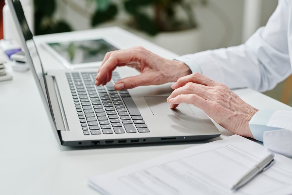 Hands of contemporary teledoc over laptop keyboard during online consultation